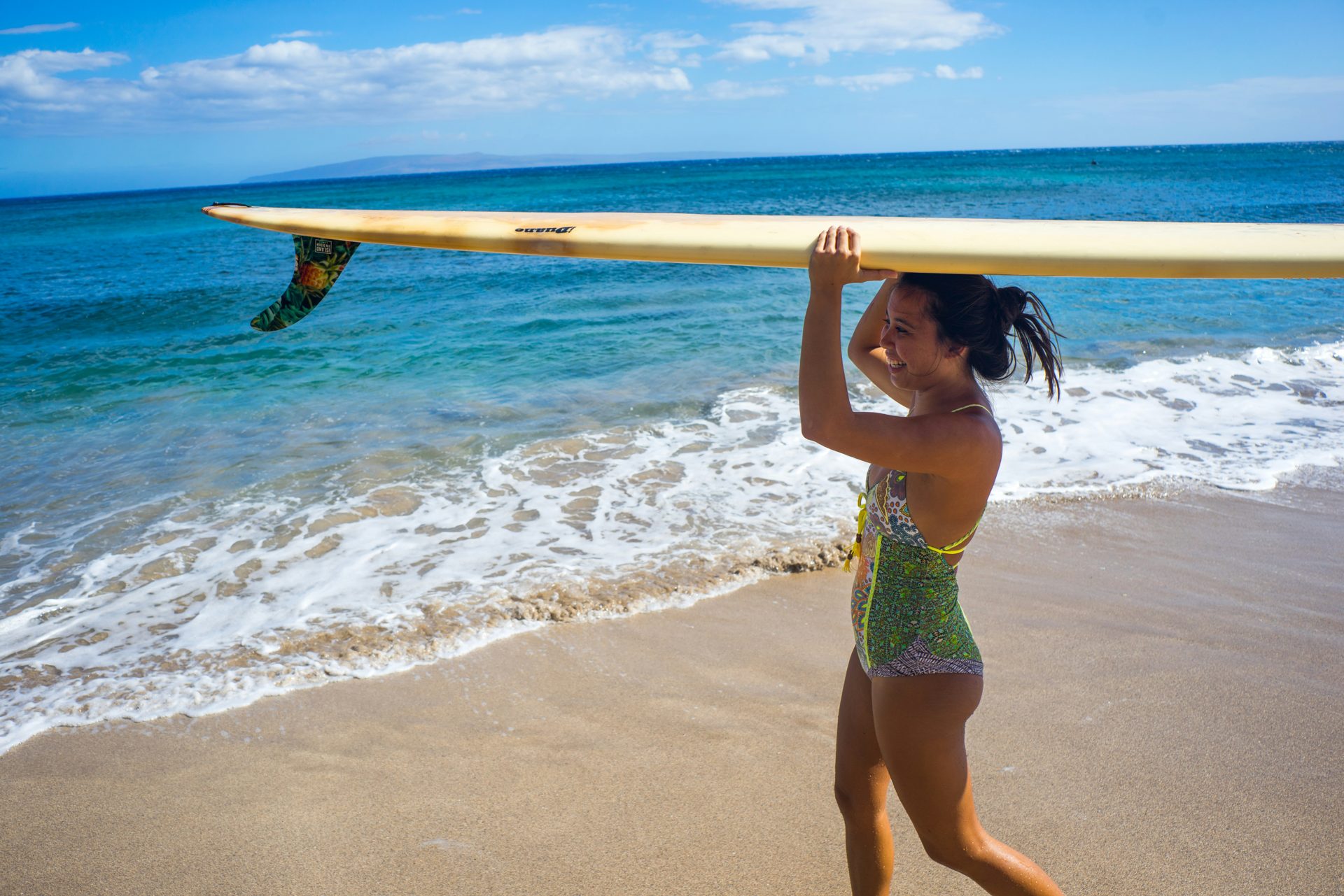 Woman carrying a longboard on the beach Travel light: board, suit, sun cream and not much else. Photo: Digital Reach A / Unsplash