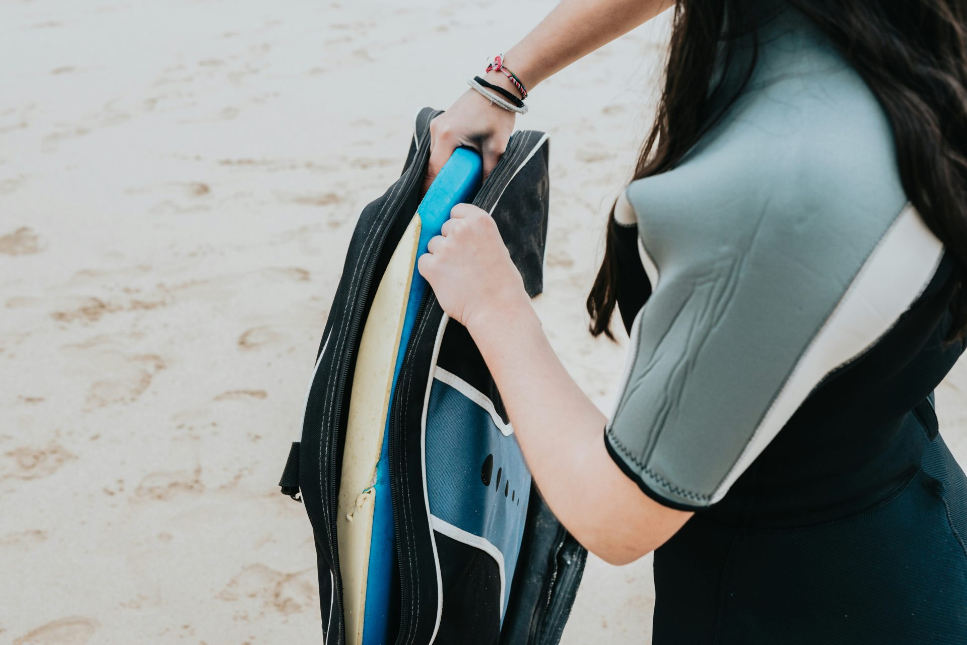 Woman in a wetsuit getting her board ready Dress for the water temperature, not the air — and get the thickness right. Photo: A C 3xnno3 / Unsplash